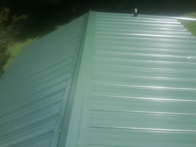 New green metal panels meeting at the ridge of a roof — Flat Roof Repair work by our crew in Mount Holly