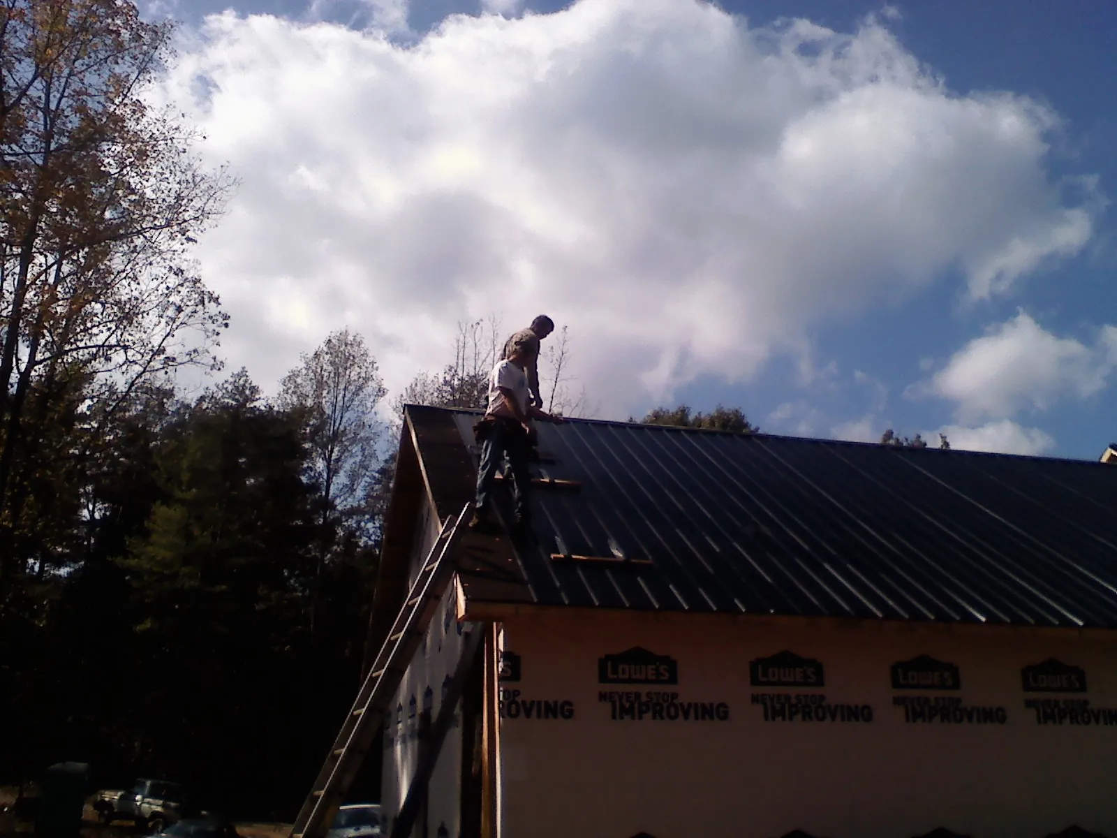 Roofer fastening dark metal panels high against a cloudy sky, from a Roof Inspection job in Mount Holly